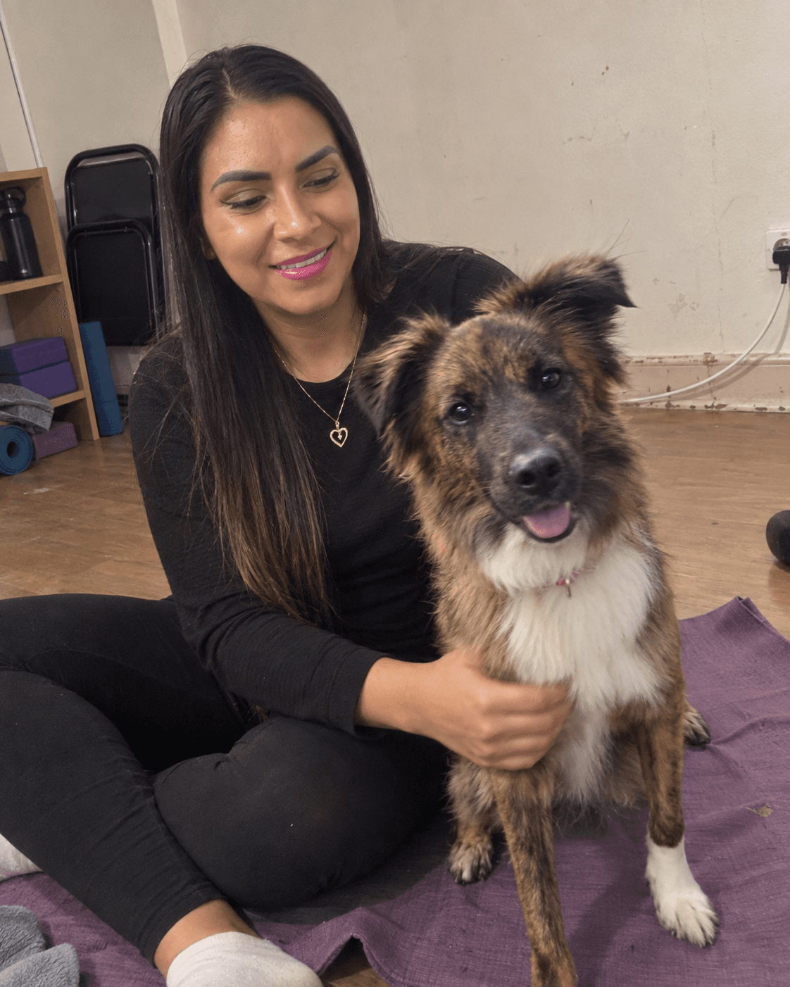 Una mujer sentada en una esterilla de yoga abraza a su perro, que mira a cámara